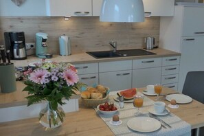 A modern kitchen with a sink, coffee maker, and breakfast setup including bread, fruit, and a vase of flowers. - Holiday apartment with 1 bedroom (Zingst)