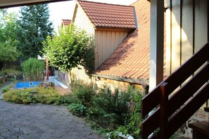 A residential building with a red-tiled roof, a wooden staircase, and a garden area with various plants and a small blue structure. - Holiday home with 4 bedrooms (Brachttal-Schlierbach)
