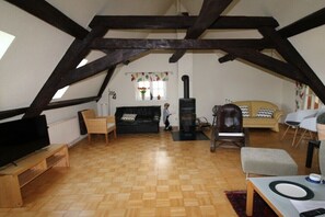 An attic room with exposed wooden beams, a fireplace, a sofa, a television, and a dining table. - Holiday home with 4 bedrooms (Brachttal-Schlierbach)
