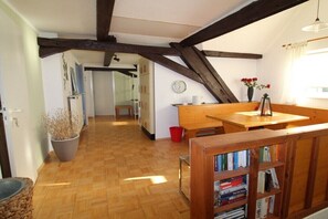 A room with wooden beams, a bookshelf, a dining table, a red bucket, and a potted plant. - Holiday home with 4 bedrooms (Brachttal-Schlierbach)