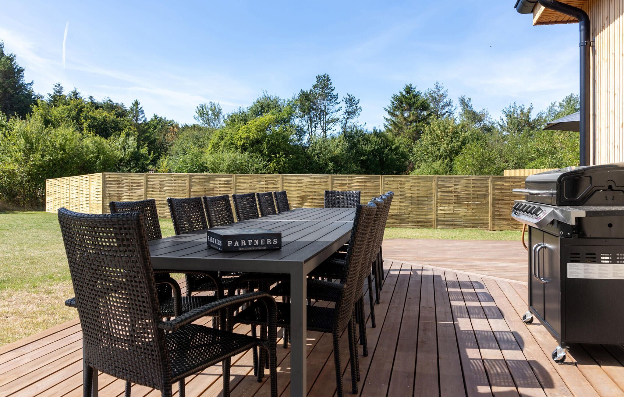 Una terraza al aire libre con una mesa de comedor y sillas, una parrilla y una valla de madera.