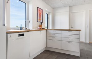 A modern kitchen with white cabinetry, a dishwasher, a countertop with a sink, and a window providing natural light.