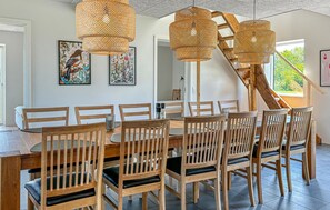 A dining area with a round table and wooden chairs, a staircase, and two framed artworks on the wall.