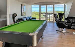 A pool table in a room with a view of the outdoors, a seating area with a sofa and chairs, and a door leading outside.