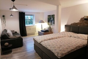 A bedroom with a bed, a sofa, a lamp, a window, and a staircase. - Holiday farmhouse with 2 bedrooms (Langenhorn)