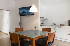 Eine moderne Küche mit weißen Schränken, einem Glastisch und einem Wand-Fernseher.