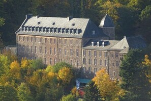 Ein großes Steinhaus mit zahlreichen Fenstern und einem markanten Turm, umgeben von Bäumen.