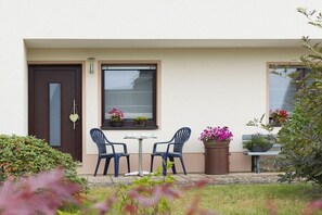 Eine kleine Terrasse mit zwei Stühlen, einem Tisch, einer Tür und einem Fenster mit einem Blumentopf.