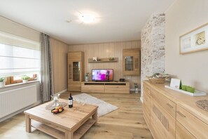 Ein modernes Wohnzimmer mit einem Holzesstisch, einem Fernseher und einer Küchenzeile mit Holdelementen und einer Wand aus Backsteinen.