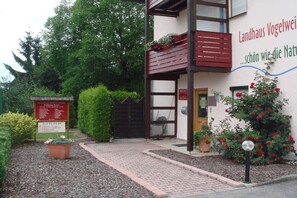 Ein Gebäude mit einem Schild für ein Wellnessangebot, einem hölzernen Balkon und einem Garten mit roten Blumen.