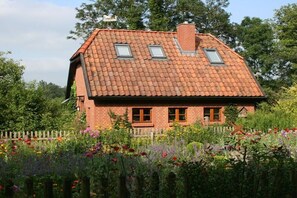 Ein Haus aus Backsteinen mit einem Ziegeldach, zwei Fenstern und einem Holzzaun im Vordergrund.