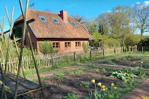 Ein Haus mit schrägem Dach, Holzzaun und einem Garten mit verschiedenen Pflanzen und Blumen.