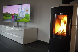 Ein modernes Wohnzimmer mit einem Flachbildfernseher, der an einem weißen Schrank befestigt ist, einem Kaminofen und einem Computerspiel zum Thema Burg auf dem Bildschirm.