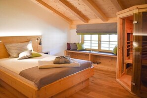 Ein Holzbett mit Kissen, eine Bank mit Polstern, ein Fenster mit Jalousien und eine Schiebetür.