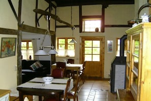 A rustic interior with exposed beams, a dining area, a kitchen with a stove, and a large window. - Cozy thatched cottage (Klocksdorf)