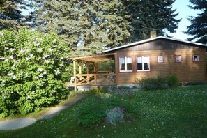 Eine Holzhütte mit Veranda, umgeben von üppiger Vegetation und Bäumen.