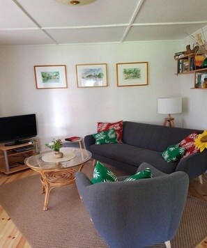 Ein Wohnzimmer mit Sofa, Sessel, TV-Schrank und an der Wand befestigten Bildern.