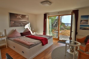 Ein Schlafzimmer mit einem Bett, einem Nachttisch, einem Tisch und Blick ins Freie.