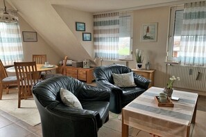 A cozy living room with a sofa, a coffee table, and a dining area with chairs and a table. - Holiday apartment in Büsum with swimming pool (Büsum)