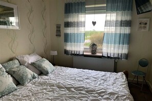 A bedroom with a bed, a chair, a window with curtains, a radiator, and wall decorations. - Holiday apartment in Büsum with swimming pool (Büsum)