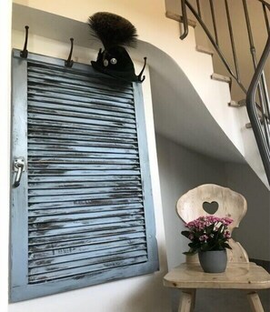 Ein blau gestrichenes Rolltor mit Herzförmigem Ausschnitt, ein kleiner Holzstuhl ebenfalls mit Herz-Ausschnitt und ein Blumentopf mit rosa Blüten.