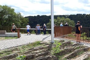 Eine Gruppe von Personen auf einem gepflasterten Weg mit Geländer, mit Blick auf einen bewaldeten Hügel.