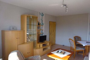 Ein Wohnzimmer mit Holzschrank, Fernseher, Esstisch und Stühlen sowie Deckenventilator.