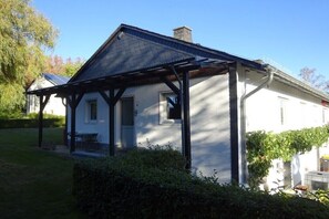 Ein weißes Haus mit Veranda, Schornstein und kleinem Garten.