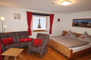 Une pièce comprenant un lit, un canapé, une chaise, une petite table et une fenêtre avec des rideaux.