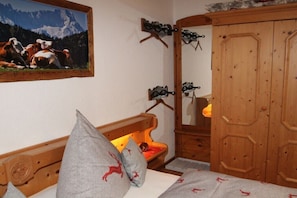 Ein Schlafzimmer mit einem Holz-Kopfteil, einem Bett mit grauer Bettwäsche, einem kleinen Nachttisch mit Lampe, einem Holzschrank und einem gerahmten Bild an der Wand.