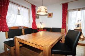 Un coin repas avec une table en bois et des chaises noires, des rideaux rouges et une lampe fixée au mur.