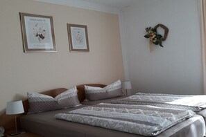 Camera d'albergo con due letti, un comodino, una lampada e due stampe incorniciate di soggetti floreali alle pareti.