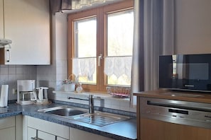 Eine Küche mit einem Spülbecken, einer Kaffeemaschine, einer Mikrowelle und einem Fenster mit Spitzenvorhängen.