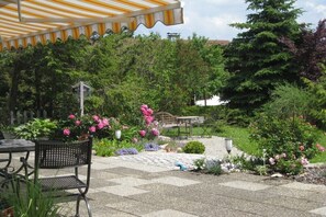 Eine Terrasse mit Tisch und Stühlen, umgeben von einem Garten mit verschiedenen Pflanzen und Blumen.