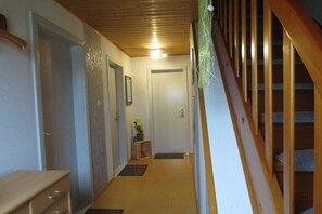 A hallway with a wooden staircase, a door, and a small shelf with a plant. - "Röben Vegetable Farm" (Zetel)
