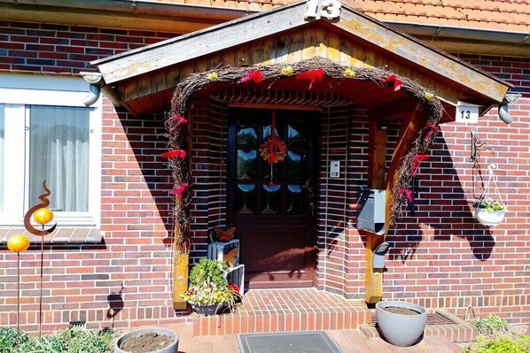A brick building with a number 13 sign, a door with a wreath, and potted plants outside. - "Röben Vegetable Farm" (Zetel)