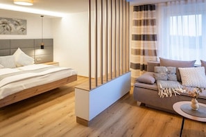 Ein modernes Schlafzimmer mit Bett, Sofa, Holzboden, Kopfteil und einer dekorativen Wandverkleidung.