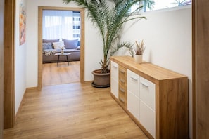 Ein Flur mit Holzboden, einem Blumentopf, einem kleinen Tisch und einer Couch im Hintergrund.