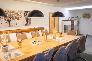 Ein Essbereich mit Holztisch, grau gepolsterten Stühlen, schwarzen Pendelleuchten und Wandbildern.