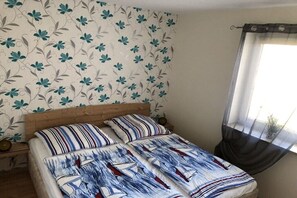 A bedroom with a bed, floral wallpaper, and a window with a sheer curtain. - Holiday apartment with 1 bedroom (Wangern)