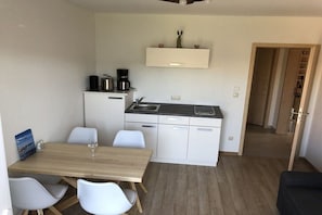 A compact kitchen with a dining area, white cabinets, a coffee machine, and a small shelf with decorative items. - Holiday apartment with 1 bedroom (Wangern)