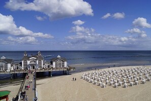 Ein Strand mit einem Steg, Strandkörben und einem Gebäude mit einem Balkon mit Blick auf das Meer.