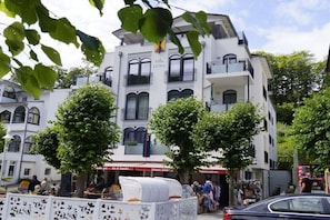 Ein mehrstöckiges Gebäude mit Balkonen, einem Schild mit der Aufschrift 'Villa LENA' und einer Straße mit Geschäften und Menschen.