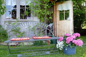A metal bench with cushions, a wooden structure with windows, and a potted plant with pink flowers. - in the Allgäu region, the Kleinert family (Argenbuehl-Eglofs)