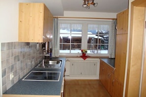 A kitchen with a double sink, wooden cabinets, a window with a view, and a radiator. - B and B with 1 bedroom (Fischen \/ Allgäu)