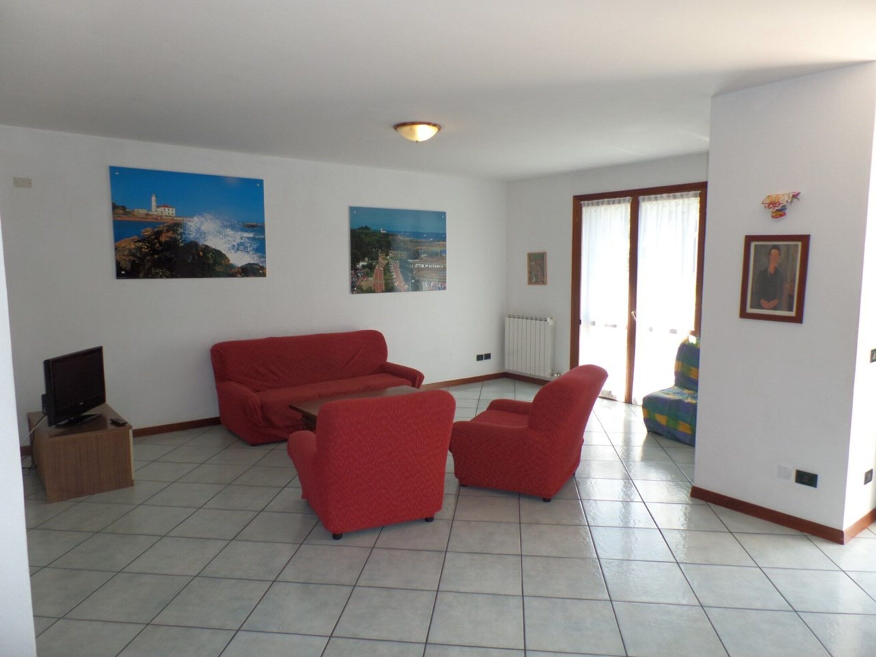 Una sala de estar con un sofá rojo, un televisor sobre un mueble bajo y dos grandes cuadros de paisajes en las paredes.