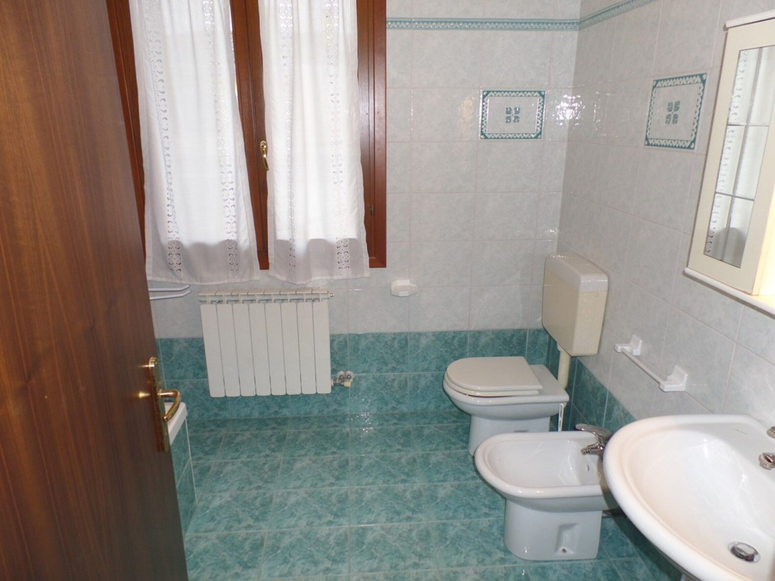 Un baño con inodoro, bidé y lavabo, suelo de baldosas y un radiador.