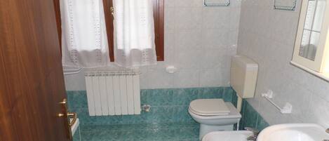 Un baño con inodoro, bidé y lavabo, suelo de baldosas y un radiador.