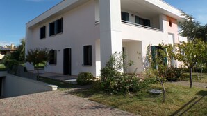 Ein modernes, zweistöckiges Haus mit flachem Dach, großen Fenstern und einem kleinen Garten mit Sträuchern und einem Baum.