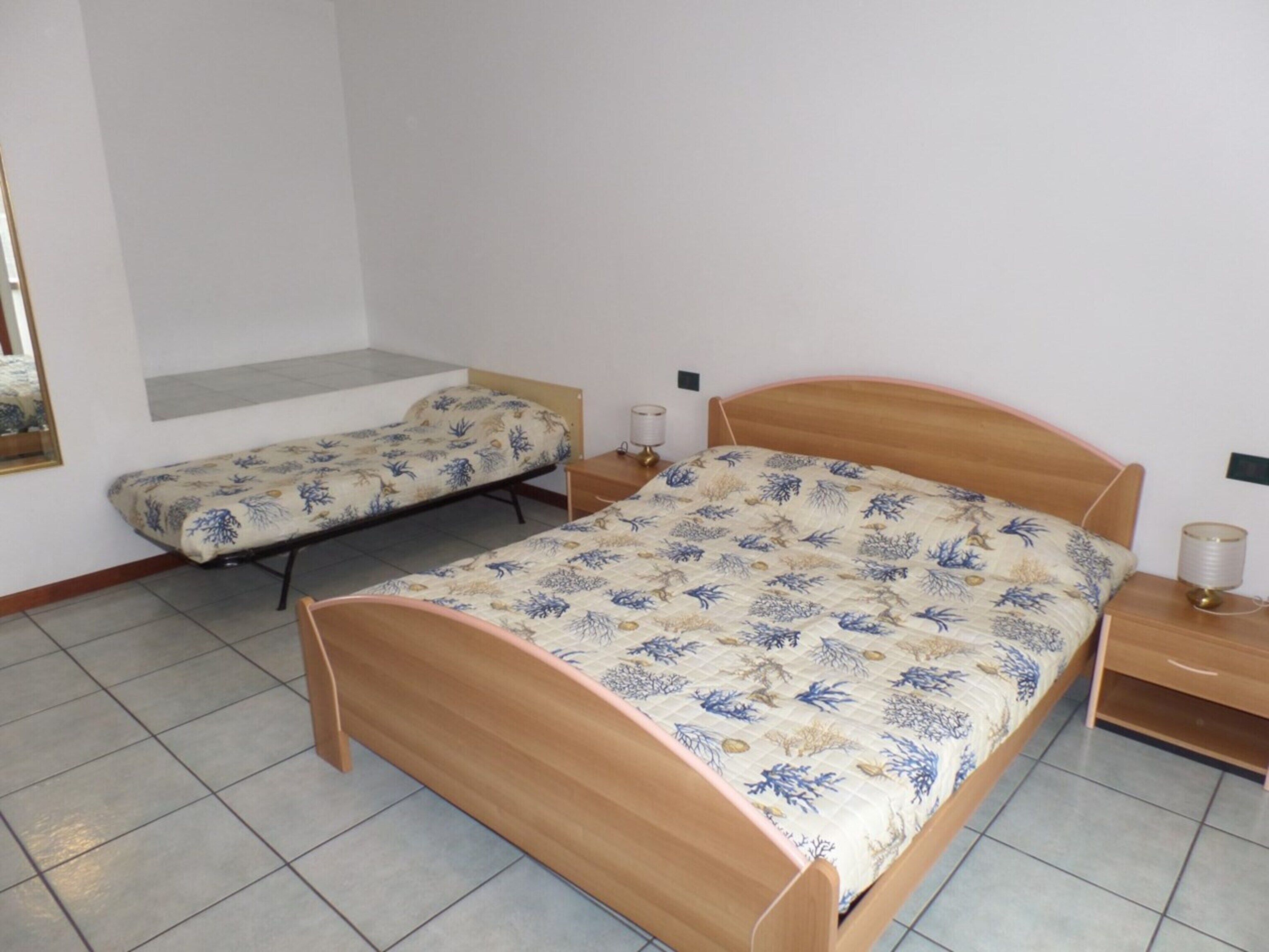 A bedroom with two single beds, a wooden headboard, a bedside table with a lamp, and a mirror on the wall.